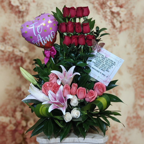 arreglo floral con rosas rojas verticales, rosas rosadas, lirios blancos y rosados, rosas blancas, globo rosa con texto te amo y tarjeta sobre fondo difuminado