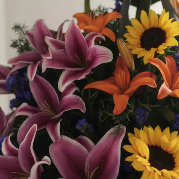 Primer plano extremo de un arreglo floral exótico con lirios rosados, lirios naranjas y girasoles amarillos, mostrando textur