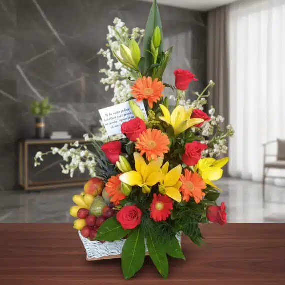 Arreglo Floral con Frutas Quitana: Elegancia y Frescura para Regalar Arreglo floral con rosas rojas, lirios amarillos, gerberas naranjas y frutas frescas en una cesta blanca, sobre una mesa de m