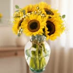 Arreglo floral de girasoles vibrantes en un jarrón de cristal transparente con lazo de yute, sobre un fondo elegante y suavem