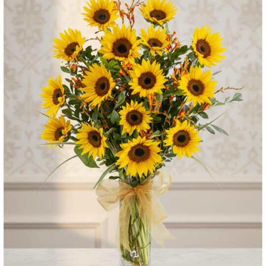 Arreglo floral de girasoles LENU en un jarrón de cristal con lazo dorado, sobre una mesa de mármol y fondo elegante.
