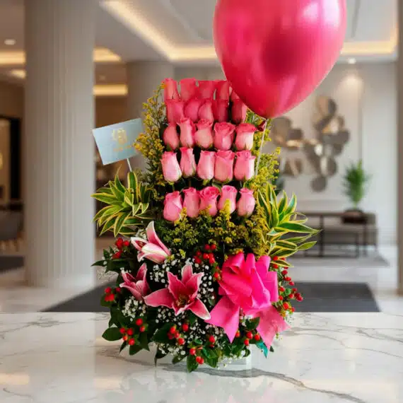 Arreglo Floral Quiero que Sepas: Rosas Rosadas y Lirios Elegantes Arreglo floral premium 'Quiero que Sepas' con rosas rosadas, lirios, follaje verde y un globo fucsia, sobre mármol en un lobb