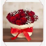 Arreglo floral 'Lidia' con 15 rosas rojas premium en un balde rústico de madera, adornado con un lazo rojo y follaje blanco,