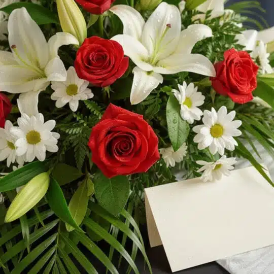 Arreglo fúnebre cubre caja Paraíso con rosas rojas, lirios blancos y margaritas, con rocío sutil y follaje verde, vista macro