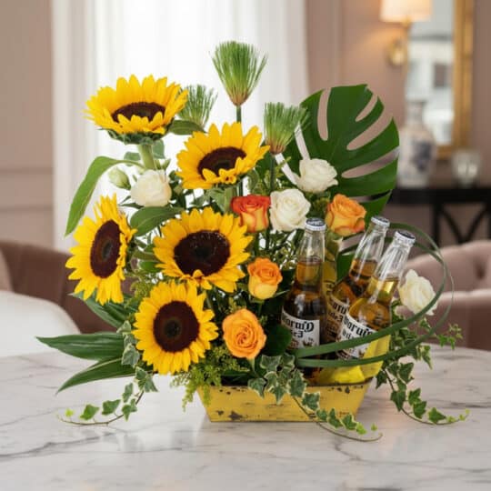 Arreglo floral vibrante con girasoles, rosas blancas y naranjas, follaje verde y tres botellas de cerveza Corona, ideal para