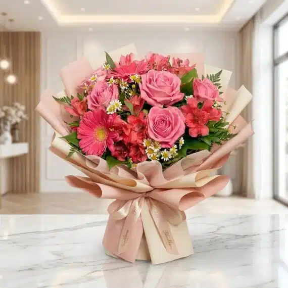 Bouquet ORLENA: Rosas Rosadas y Gerberas, Diseño Floral Primaveral Exquisito Bouquet ORLENA con rosas rosadas, gerberas fucsia y alstroemerias rojas, envuelto en papel coreano rosa claro sobre mármol bl