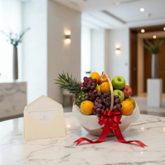 Canasta de frutas premium con piña, uvas, manzanas y naranjas, decorada con un lazo rojo y una tarjeta de regalo elegante, so
