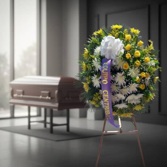 Corona fúnebre 'Estamos Contigo' con flores amarillas y blancas, cinta morada, en sala de velación moderna con ataúd desenfoc