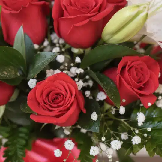 Primer plano extremo de un arreglo floral 'Jarrón Otoño' con rosas rojas vibrantes, lirios blancos y follaje verde, con sutil