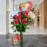 Arreglo floral Solitario con Rosas Me Enamoras, rosas rojas y una rosa blanca, follaje verde, globo de corazón 'Te Amo' y caj