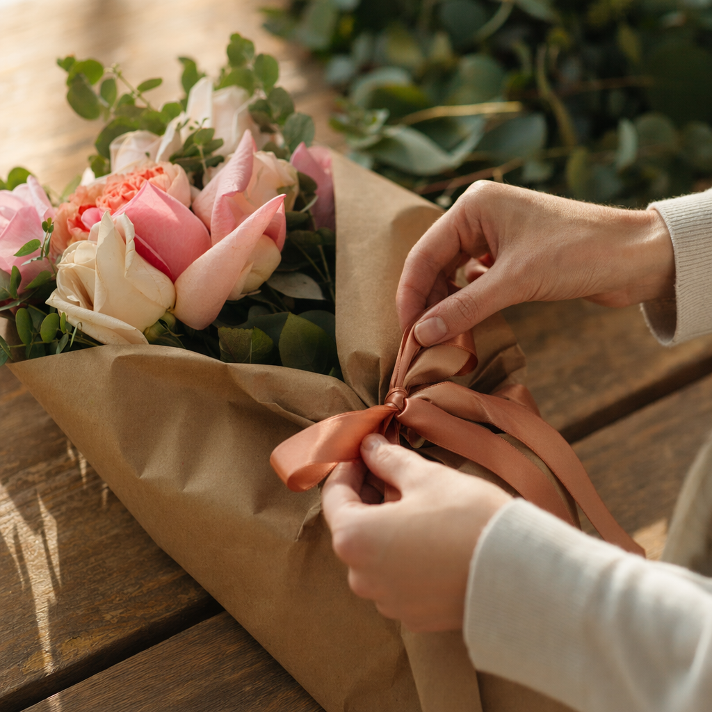 Manos envolviendo un ramo de rosas rosadas en papel kraft